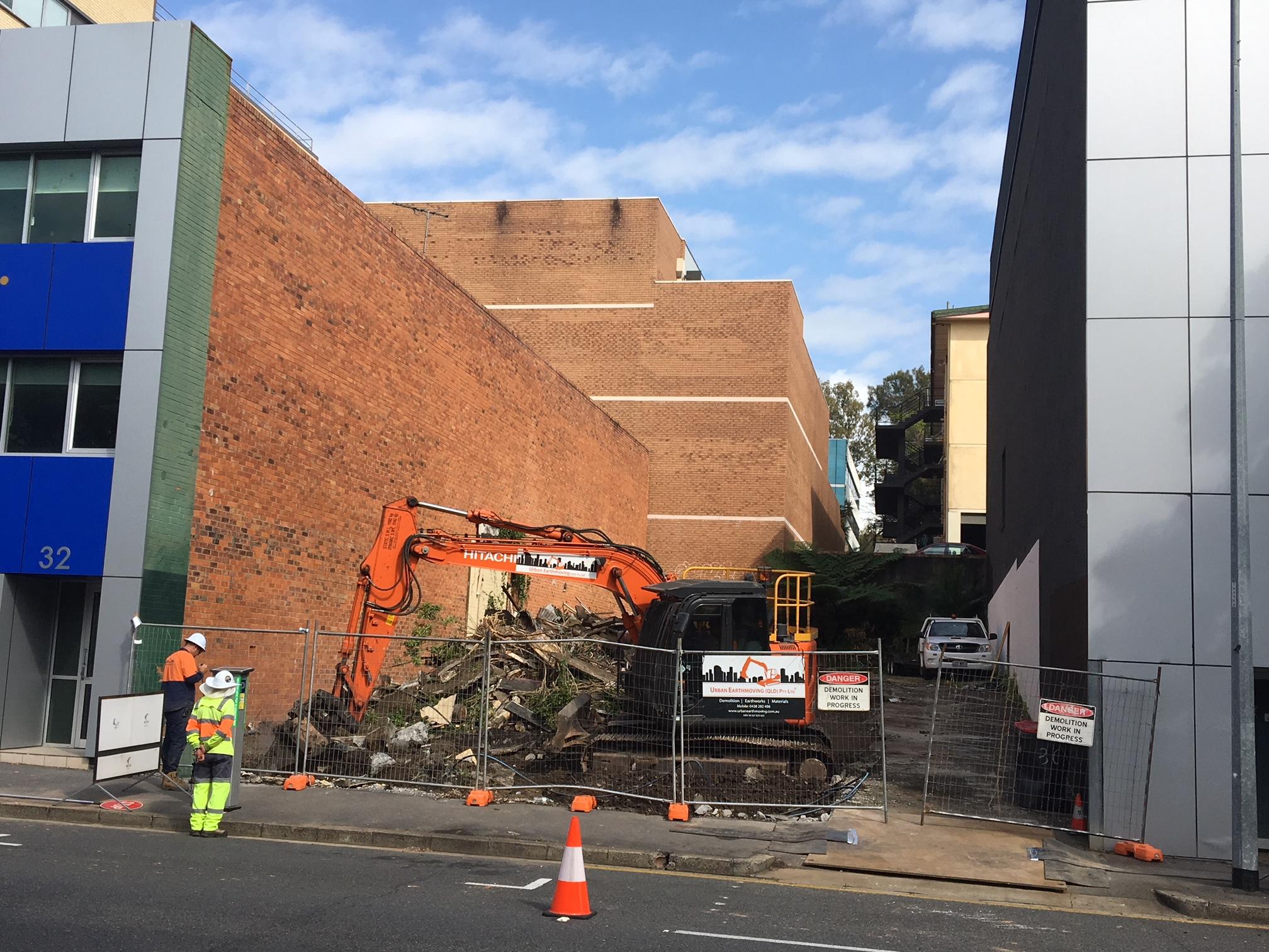 Brisbane CBD Demolition Fenced off demolition site with an orange excavator in the background