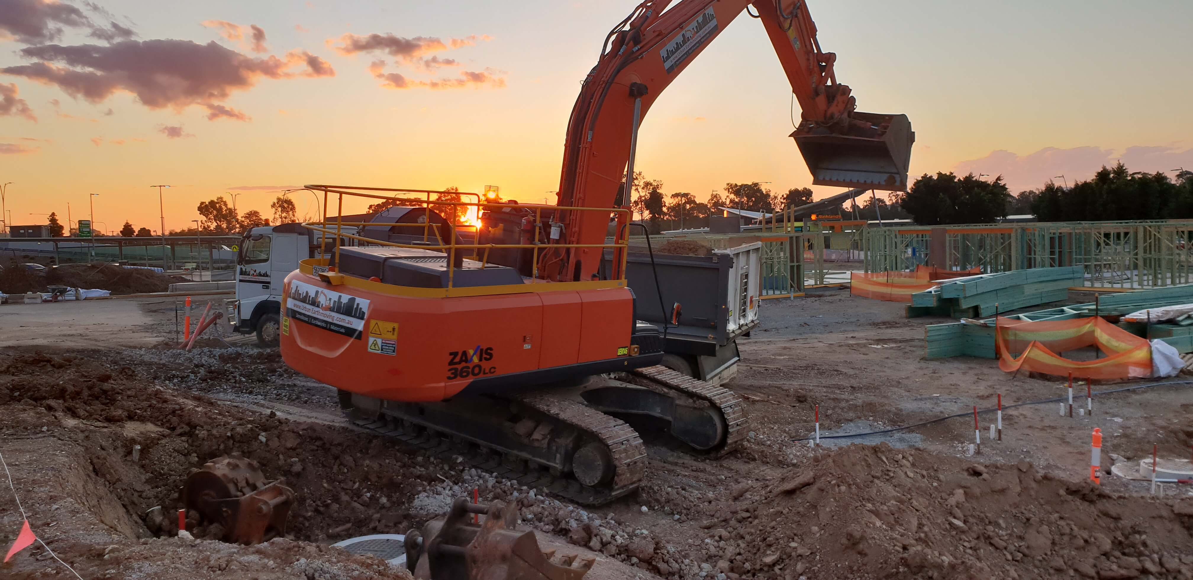 An orange excavator from Urban Earthmoving in a demolished site before sunset