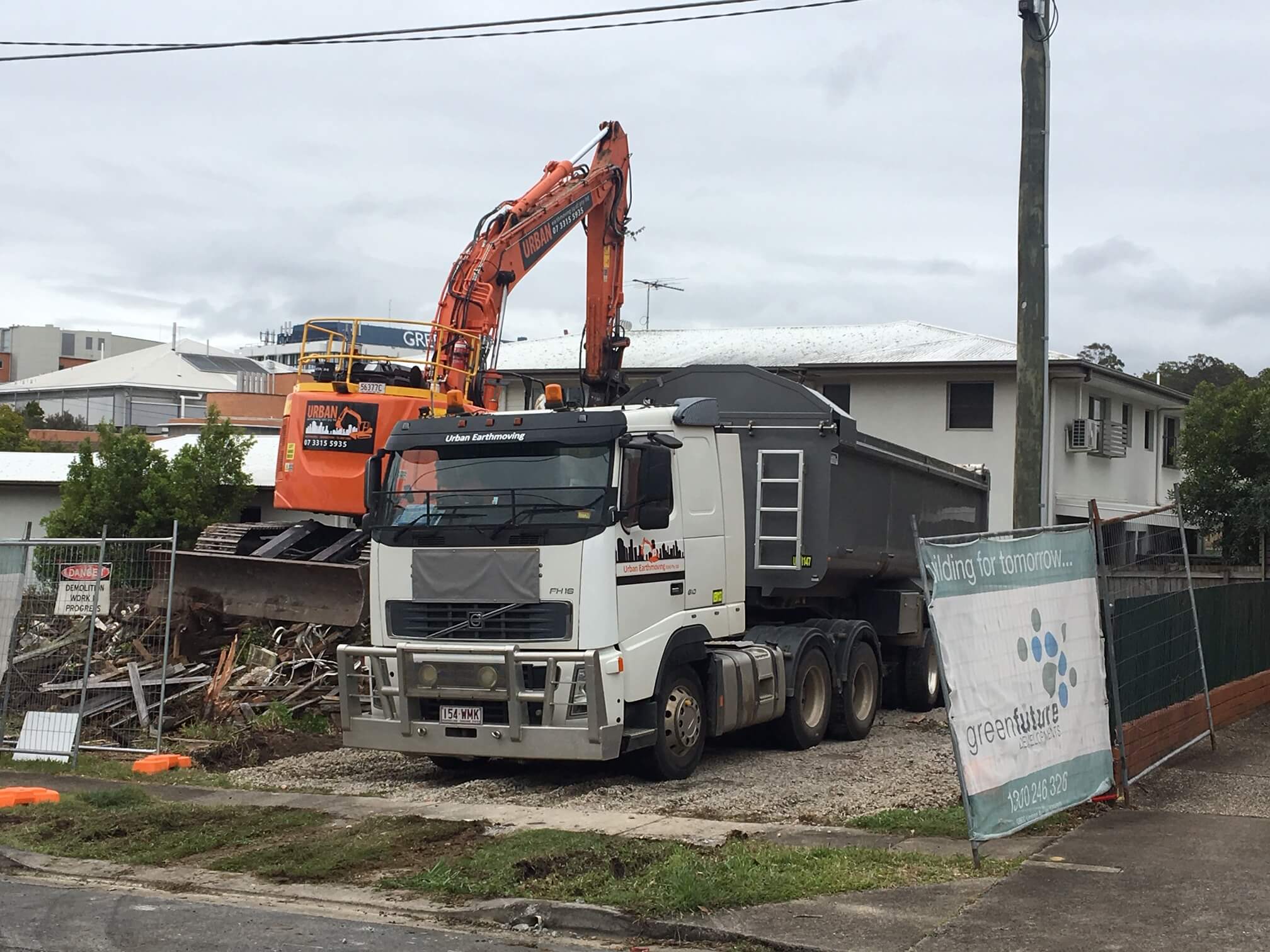 An excavator unloading debris from a demolished house into the back of a truck