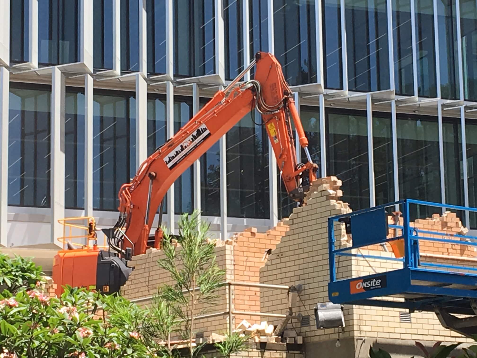 A large orange excavator demolishing a brick building