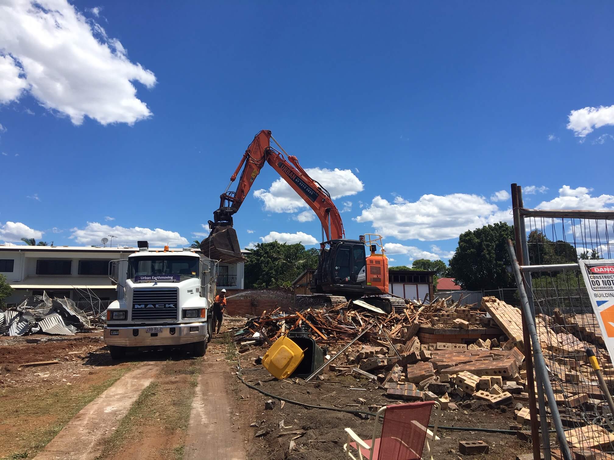 An excavator unloading debris from a demolished brick house into the back of a truck