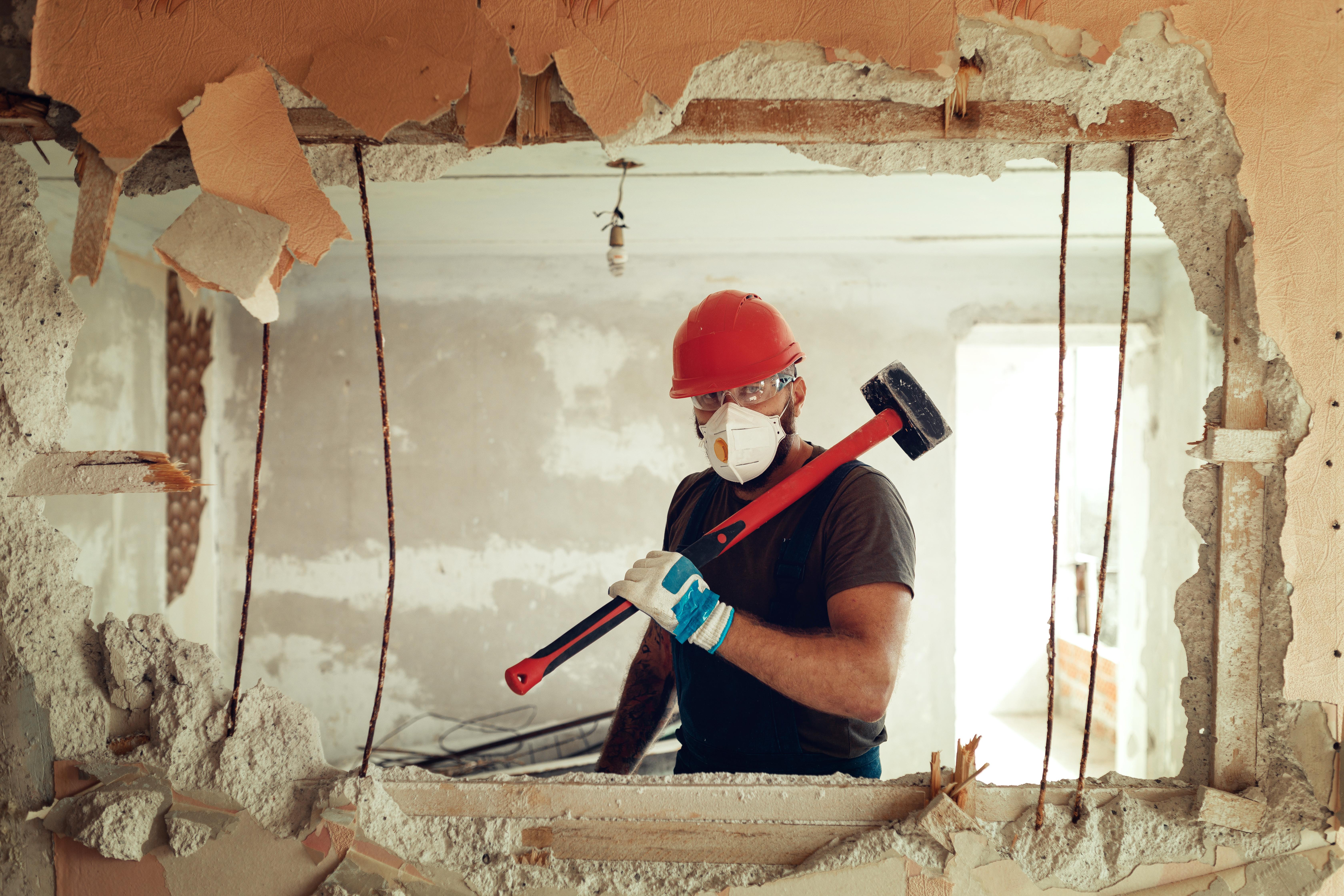 Demolition Services Brisbane Worker in protective gear with sledge hammer after demolishing through wall