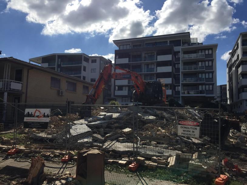 3 Storey Apartment Complex Demolition Fenced off demolition site with a large excavator in the background